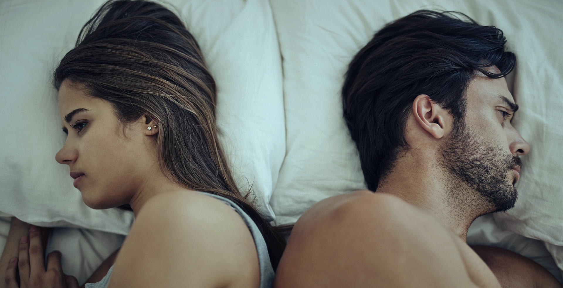 High angle shot of an arguing couple with their backs turned on each other in bed